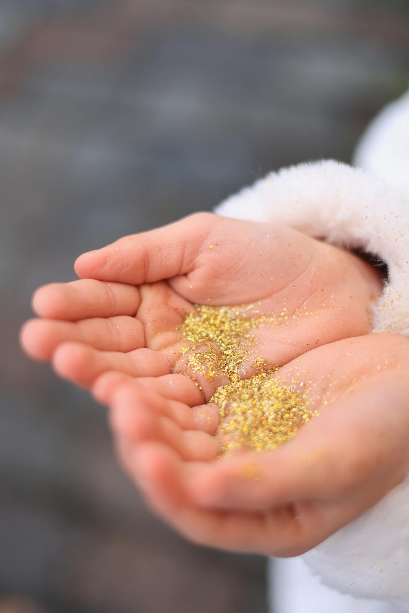 Close-up of child's hands holding scattered golden glitter, creating a warm and festive feel.