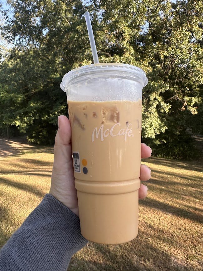 McCafé iced pumpkin spice latte held outside against fall trees